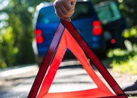 Close-up of a hand placing an emergency warning triangle by a car.
