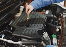 Close-up of a person checking engine oil using a dipstick in a car's engine bay.